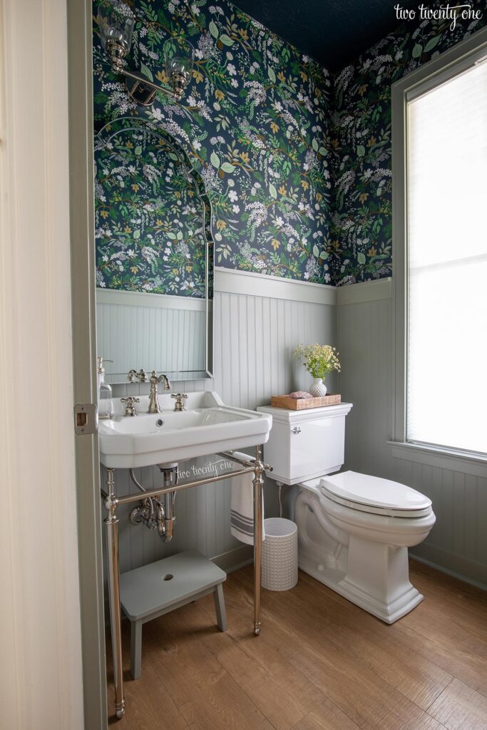 powder room with console sink, toilet, beadboard painted benjamin moore oil cloth on the bottom, rifle paper co juniper forest wallpaper on top